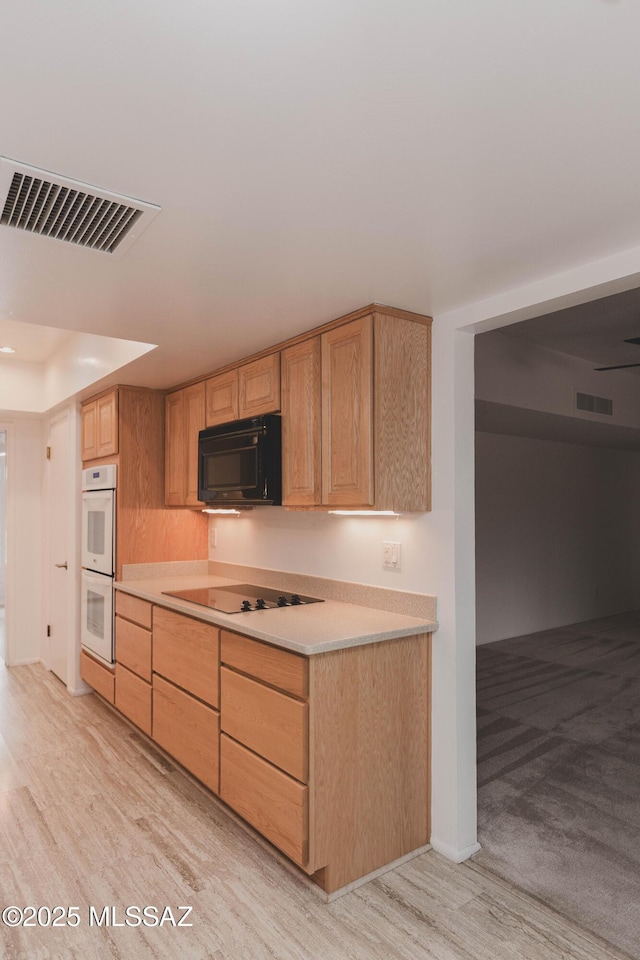 kitchen with light countertops, light brown cabinets, visible vents, and black appliances