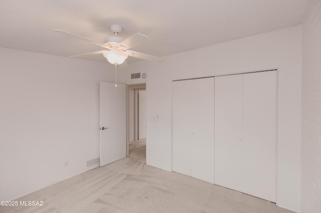 unfurnished bedroom with a textured ceiling, ceiling fan, light colored carpet, visible vents, and a closet