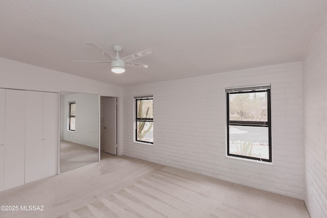 unfurnished bedroom with carpet floors, brick wall, a ceiling fan, and a textured ceiling