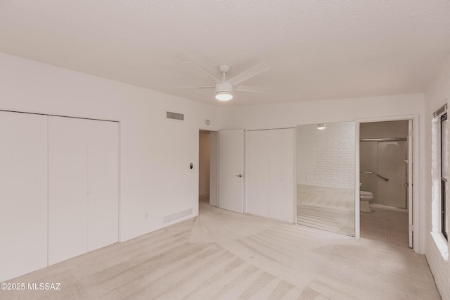 unfurnished bedroom with a textured ceiling, connected bathroom, light colored carpet, visible vents, and two closets