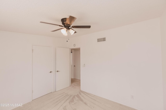 empty room featuring a ceiling fan, light colored carpet, visible vents, and a textured ceiling