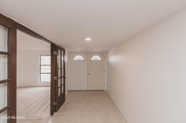 foyer entrance featuring light carpet, light tile patterned floors, a textured ceiling, and french doors