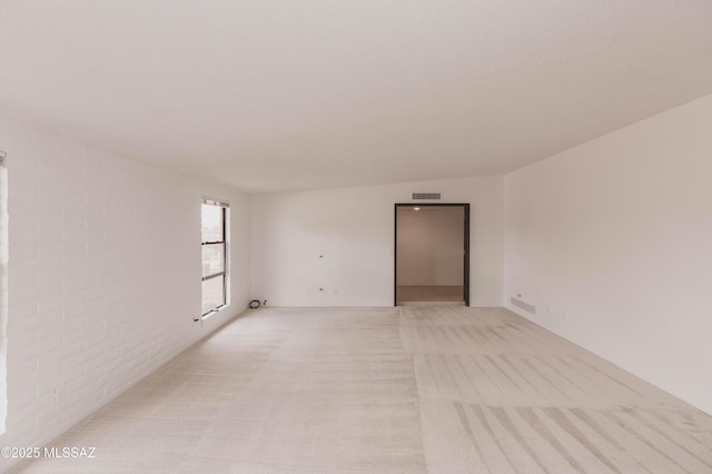 spare room with light carpet, brick wall, and visible vents