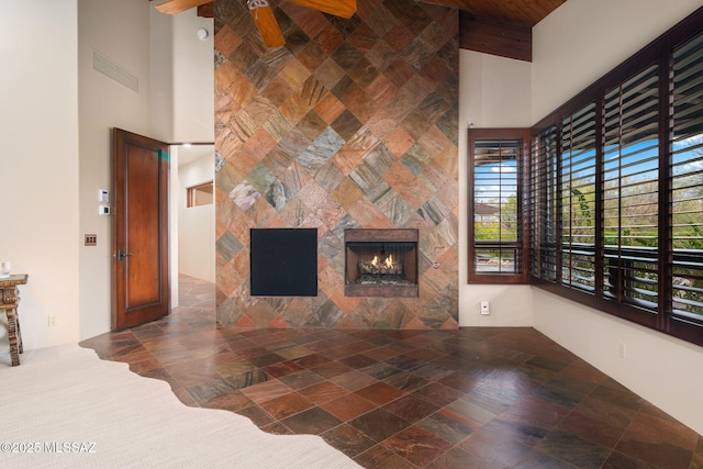 unfurnished living room with ceiling fan, a large fireplace, and a high ceiling