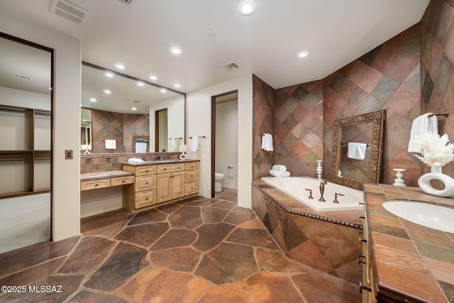 bathroom featuring tile walls, toilet, vanity, and tiled tub