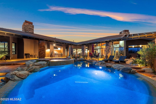 pool at dusk with an in ground hot tub