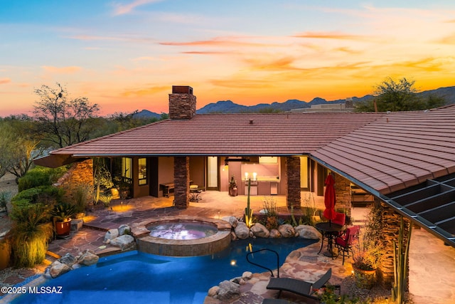 back house at dusk featuring a patio, a mountain view, and a pool with hot tub