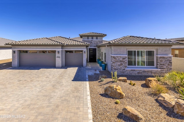 view of front of house featuring decorative driveway, a tile roof, stucco siding, an attached garage, and stone siding