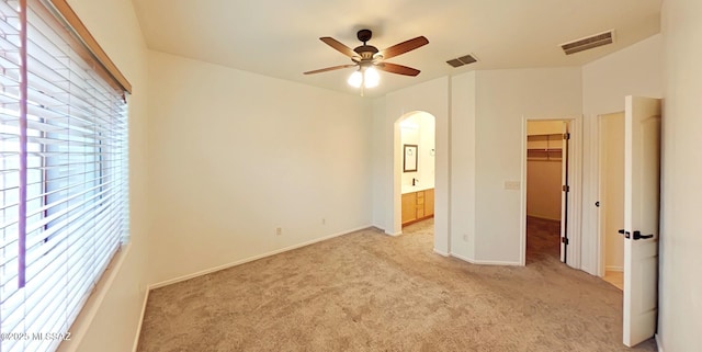 unfurnished bedroom with ceiling fan, ensuite bathroom, a walk in closet, light colored carpet, and a closet