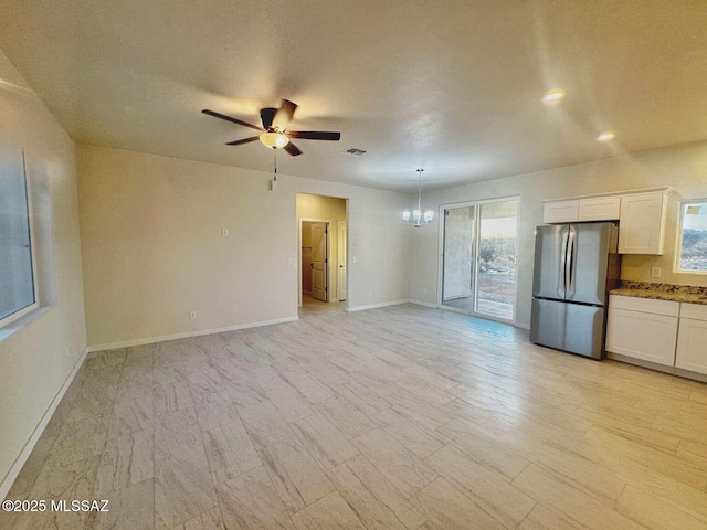unfurnished living room featuring baseboards, ceiling fan with notable chandelier, and a healthy amount of sunlight