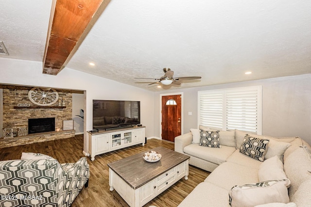 living room featuring ceiling fan, hardwood / wood-style floors, a fireplace, lofted ceiling with beams, and a textured ceiling