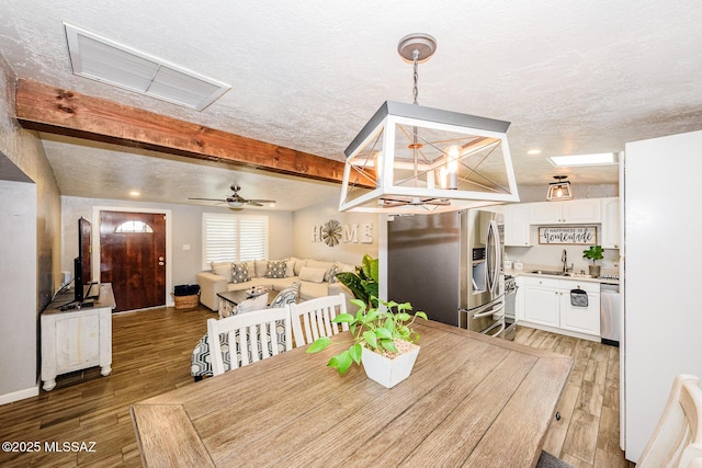 dining space with beamed ceiling, sink, a textured ceiling, and dark hardwood / wood-style flooring