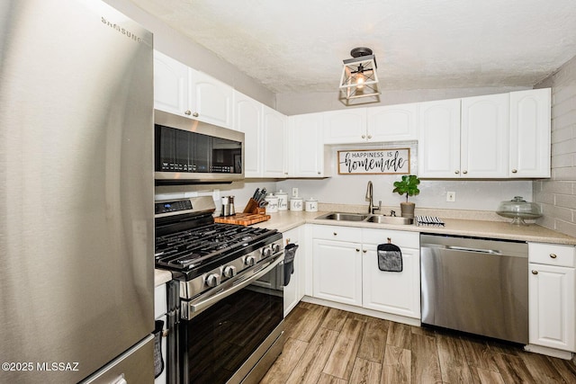 kitchen with appliances with stainless steel finishes, sink, white cabinets, light hardwood / wood-style floors, and a textured ceiling