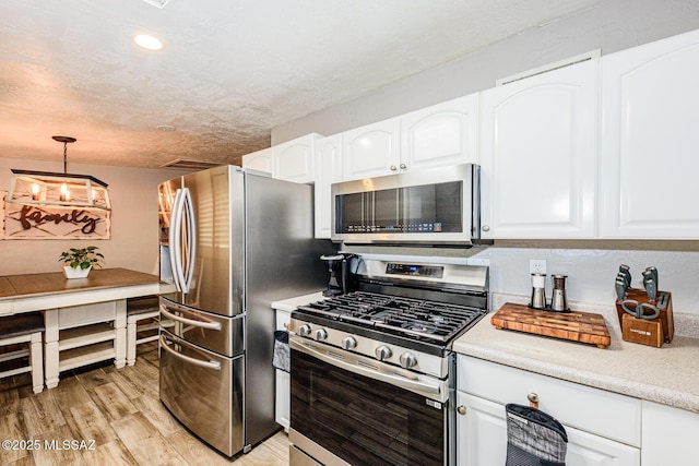 kitchen with decorative light fixtures, a textured ceiling, light wood-type flooring, appliances with stainless steel finishes, and white cabinets