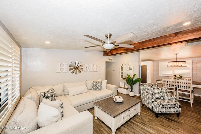 living room featuring beam ceiling, ceiling fan with notable chandelier, dark wood-type flooring, and a textured ceiling