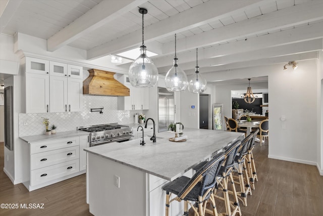 kitchen with premium range hood, decorative light fixtures, double oven range, a kitchen island with sink, and light stone countertops