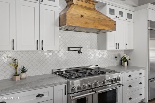 kitchen featuring backsplash, premium appliances, light stone countertops, custom range hood, and white cabinets