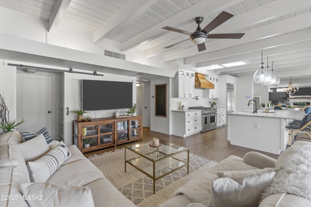 living room with sink, ceiling fan, beam ceiling, dark hardwood / wood-style flooring, and a barn door