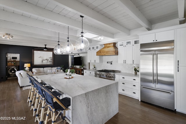 kitchen featuring high end appliances, light stone countertops, white cabinets, decorative light fixtures, and custom exhaust hood