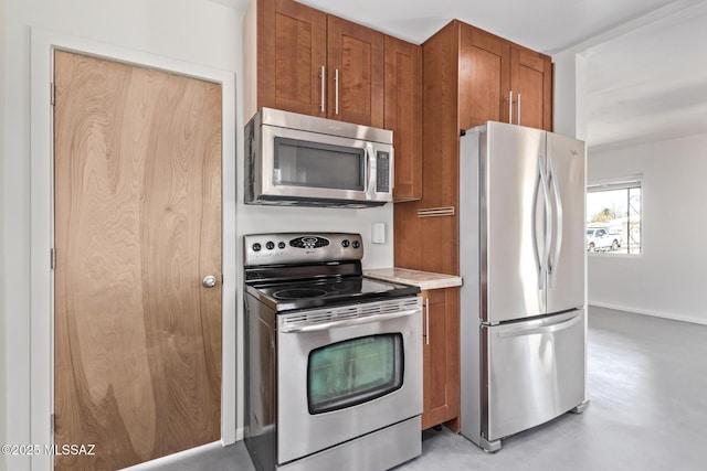 kitchen with stainless steel appliances, brown cabinetry, light countertops, concrete flooring, and baseboards