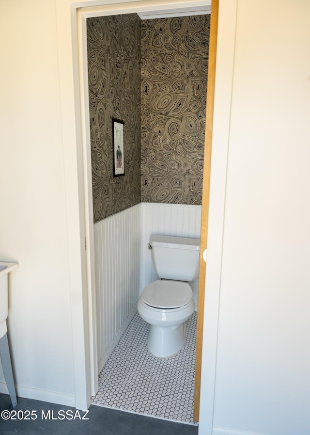bathroom featuring toilet, tile patterned flooring, wainscoting, and wallpapered walls