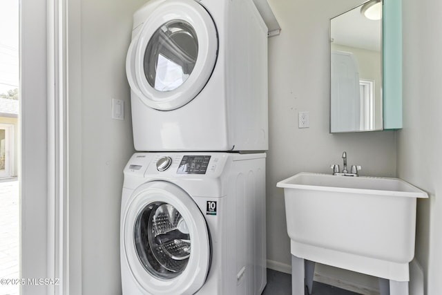 washroom featuring stacked washing machine and dryer, a sink, and baseboards