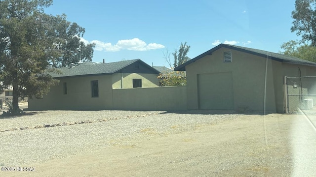 view of side of home with dirt driveway, stucco siding, a garage, and fence