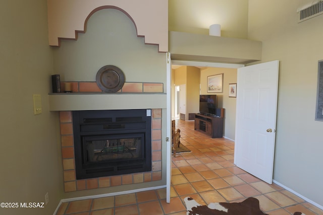 unfurnished living room with visible vents, a towering ceiling, a glass covered fireplace, baseboards, and tile patterned floors