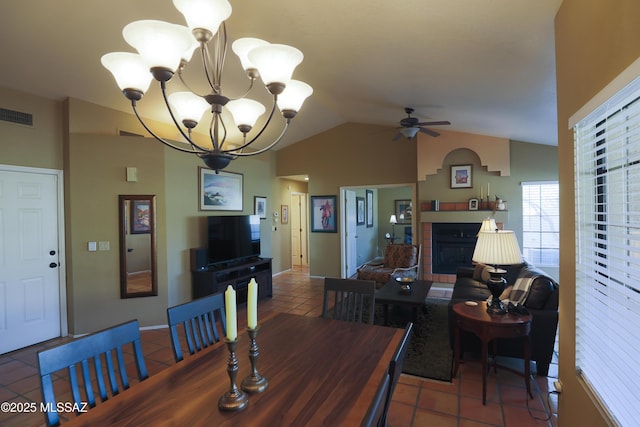 tiled dining area with a fireplace, visible vents, vaulted ceiling, and ceiling fan with notable chandelier