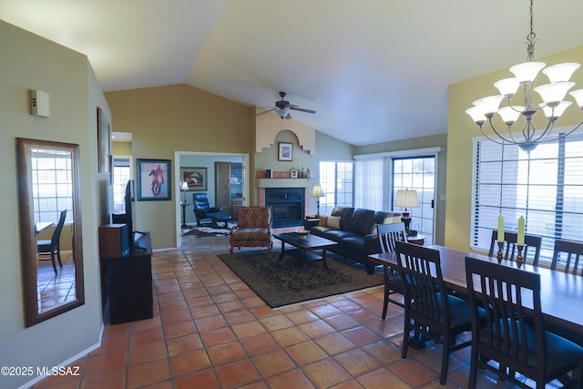 tiled dining space featuring vaulted ceiling, a fireplace, baseboards, and ceiling fan with notable chandelier