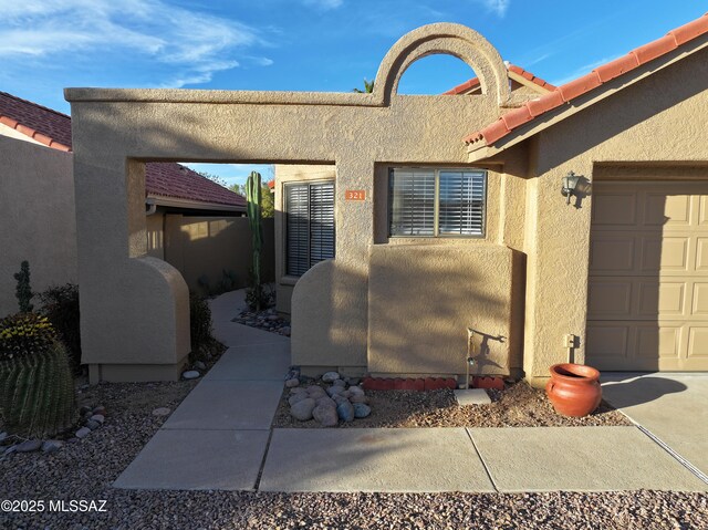 entrance to property featuring a garage, a tiled roof, and stucco siding