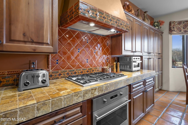 kitchen featuring stainless steel appliances, custom exhaust hood, light tile patterned floors, and backsplash