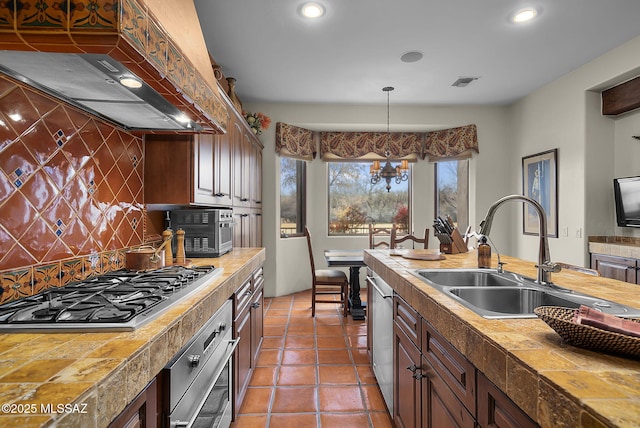 kitchen with sink, decorative backsplash, hanging light fixtures, stainless steel appliances, and custom range hood