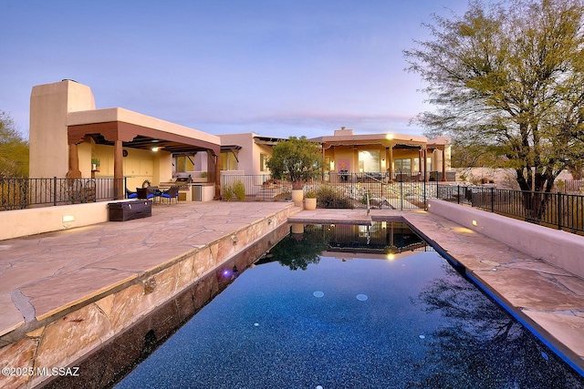 pool at dusk featuring fence, a fenced in pool, and a patio