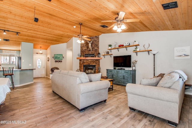 living area with lofted ceiling, visible vents, light wood-style floors, wood ceiling, and a stone fireplace