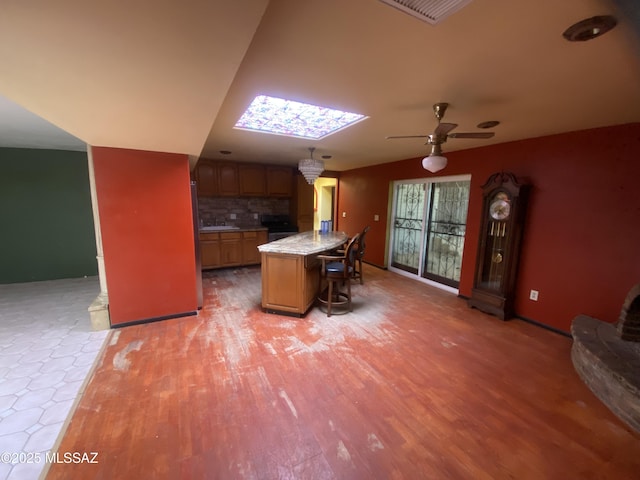 kitchen featuring hardwood / wood-style floors, a skylight, a kitchen bar, decorative backsplash, and a center island