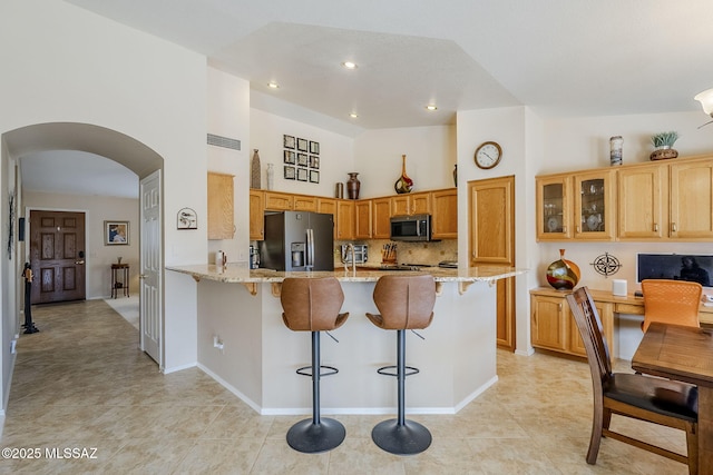 36425 S Golf Course Dr, Tucson, AZ 85739 - kitchen with light stone countertops, a peninsula, arched walkways, appliances with stainless steel finishes, and a kitchen breakfast bar