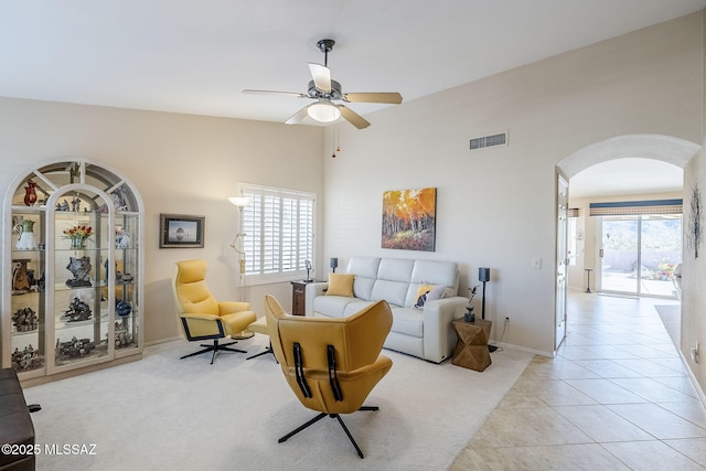 tiled living room with a wealth of natural light, visible vents, arched walkways, and a ceiling fan