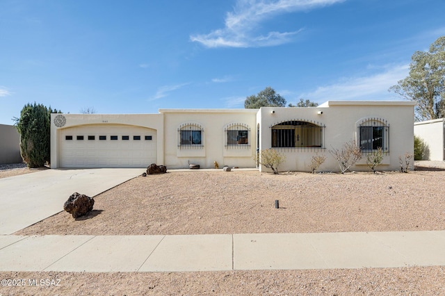 pueblo-style home featuring a garage, concrete driveway, and stucco siding