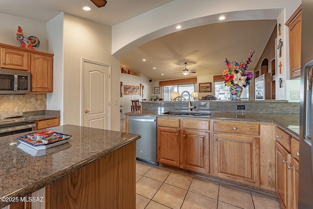 kitchen with appliances with stainless steel finishes, sink, dark stone countertops, ceiling fan, and kitchen peninsula