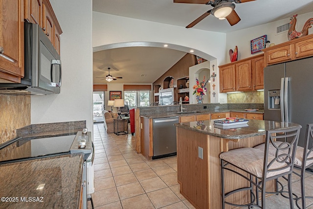 kitchen with sink, a breakfast bar area, appliances with stainless steel finishes, a kitchen island, and light tile patterned flooring