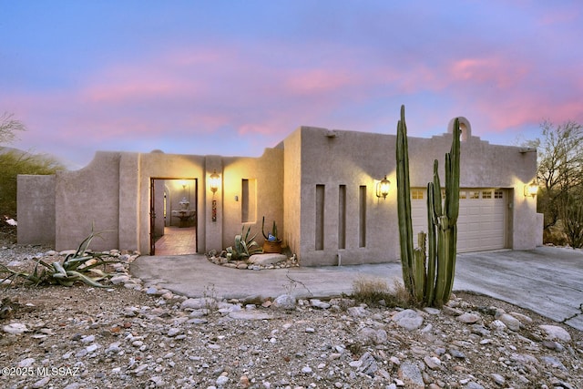 pueblo revival-style home featuring driveway, an attached garage, and stucco siding