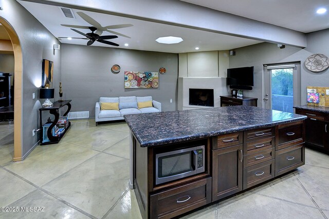 kitchen with arched walkways, visible vents, open floor plan, dark stone counters, and stainless steel microwave