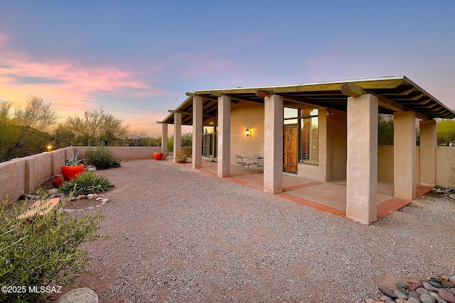 back of house at dusk featuring a patio, fence, and stucco siding