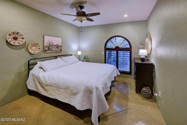 bedroom featuring finished concrete floors, a textured wall, and a ceiling fan