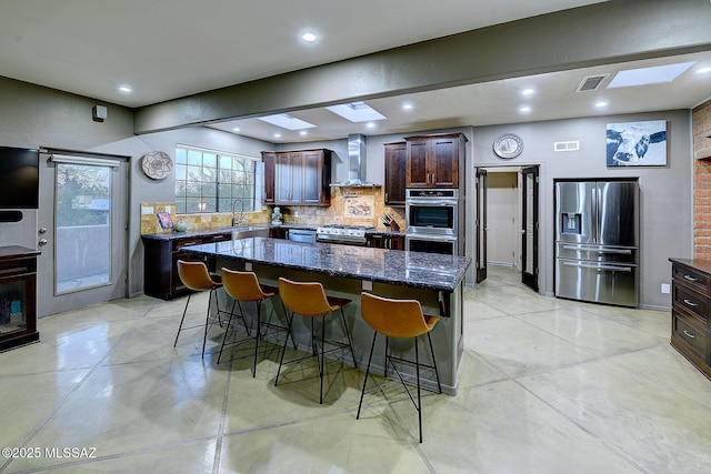 kitchen featuring wall chimney exhaust hood, appliances with stainless steel finishes, visible vents, and a kitchen breakfast bar