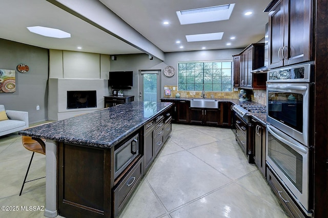 kitchen featuring a skylight, a breakfast bar area, open floor plan, a sink, and dark stone counters