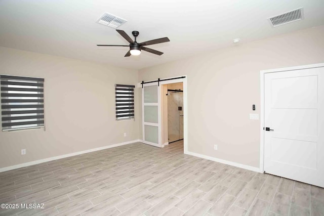 empty room with ceiling fan, a barn door, and light hardwood / wood-style floors