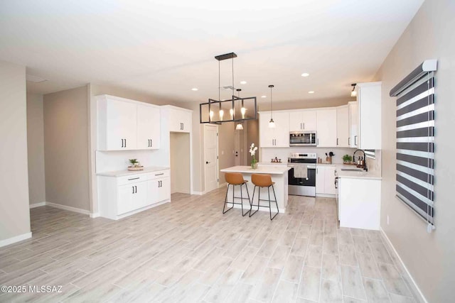 kitchen featuring sink, appliances with stainless steel finishes, white cabinetry, hanging light fixtures, and a kitchen island