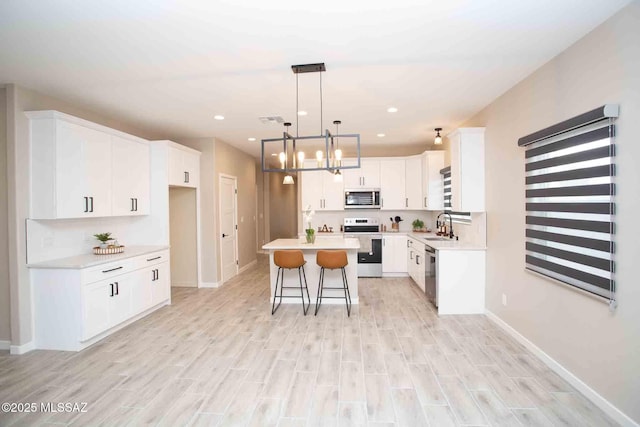 kitchen with pendant lighting, sink, appliances with stainless steel finishes, white cabinetry, and a center island